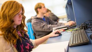 A red headed female student sits at a computer entering information.